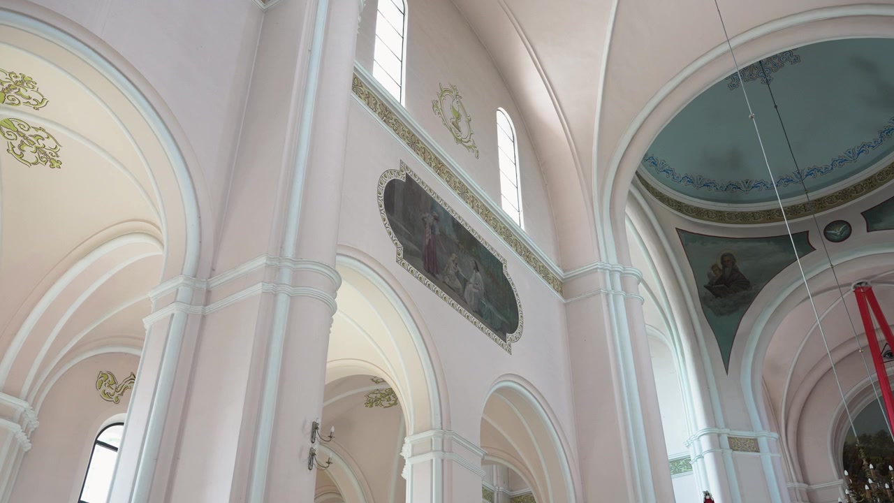 Panorâmica Ampla de um Interior de Igreja Ornamentado Apresentando Tetos Arqueados em Tons Pastel, Afrescos Decorativos, Colunas Clássicas, Lustre e Luz Natural do Dia Entrando por Janelas Altas