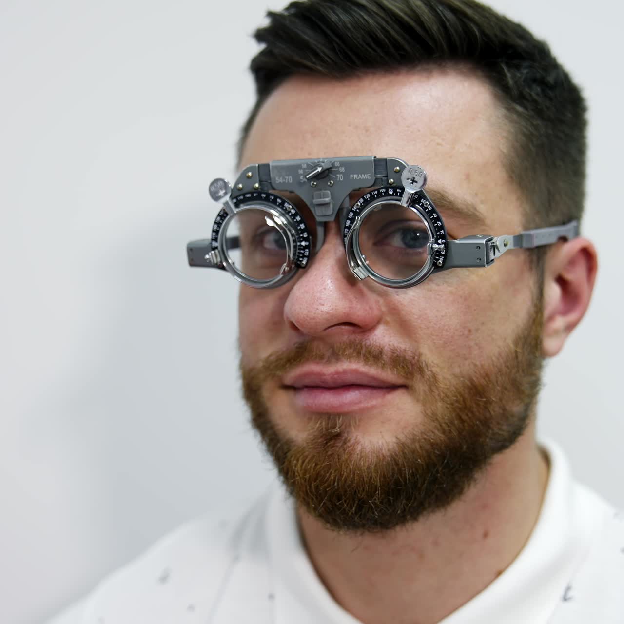 Portrait of a young bearded man in testing glasses. Patient examining his eyesight with optical trial frame in clinic. Ophthalmology concept