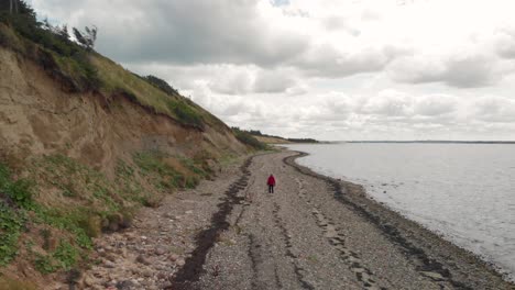 Aerial:-Woman-walking-down-beach-on-a-cloudy-day