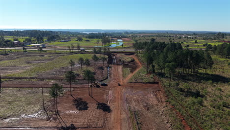 wide aerial view of rural construction site with dirt roads, trees and clear blue sky