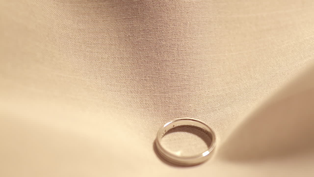 Dropping a pair of platinum engagement rings studded in diamonds on a piece of cottony cloth as it settles in the middle of the fabric