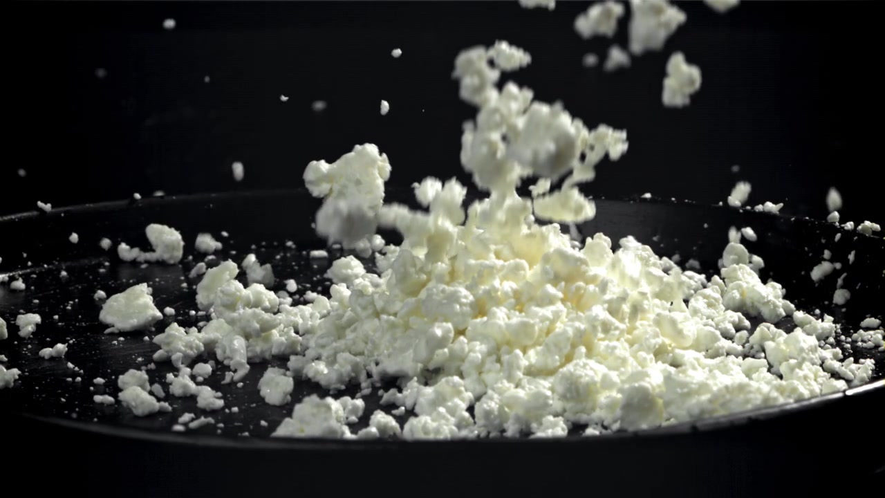 Movimento rallentato di formaggio feta friabile che cade su una superficie nera