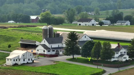 rural american farm with white barns, silos and green fields in summer. idyllic countryside scene with scattered farmhouses – classic midwest farmland. aerial view. quiet suburb district of pa, usa.