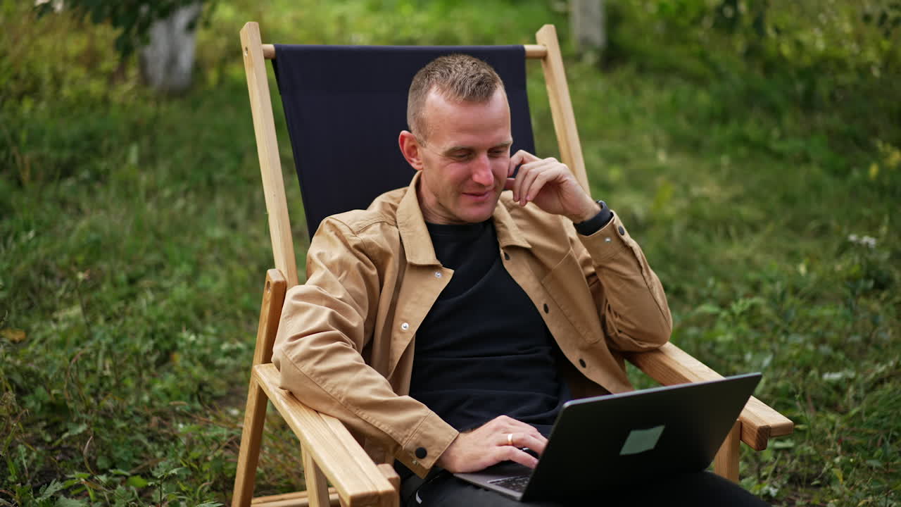 Positive laughing man working remotely having online conversation. Freelance specialist doing his job far from office in the nature.