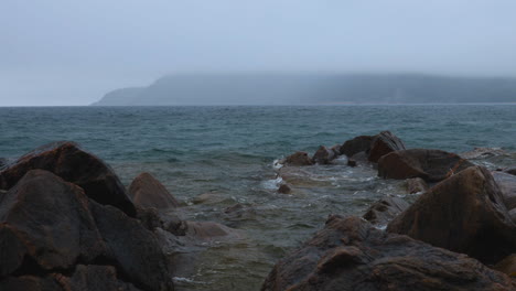 handheld shot of small waves lapping the rocky shoreline of lake superior in the rain