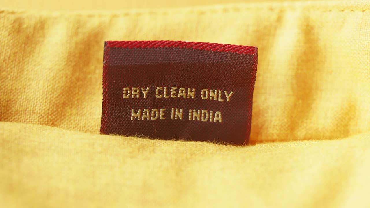 Close-up of a clothing label with 'Dry Clean Only' and 'Made in India' on yellow fabric