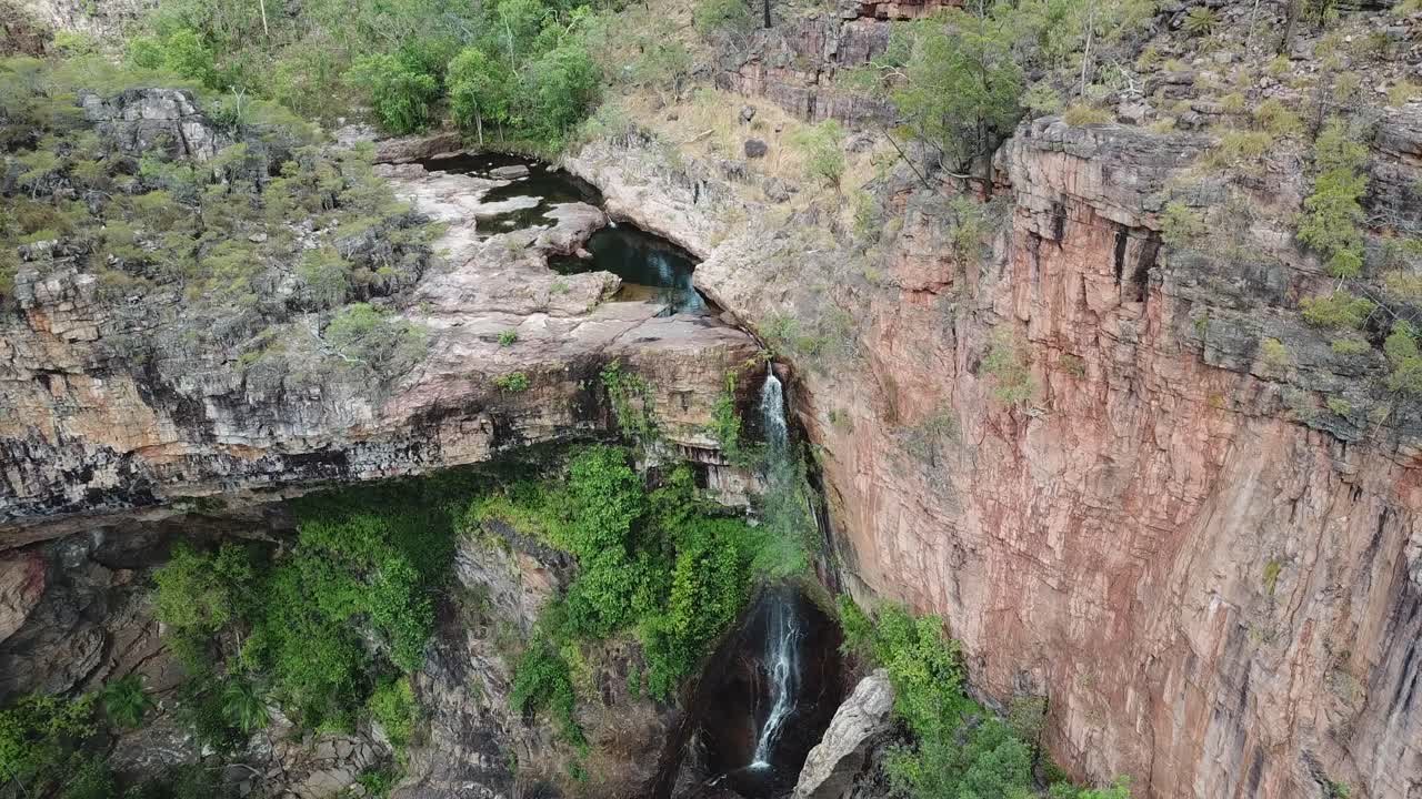 Drone footage of Sandy Creek Falls in the Northern Territory, Australia, showcasing cascading water, rugged rock formations, and lush surrounding nature in a remote landscape