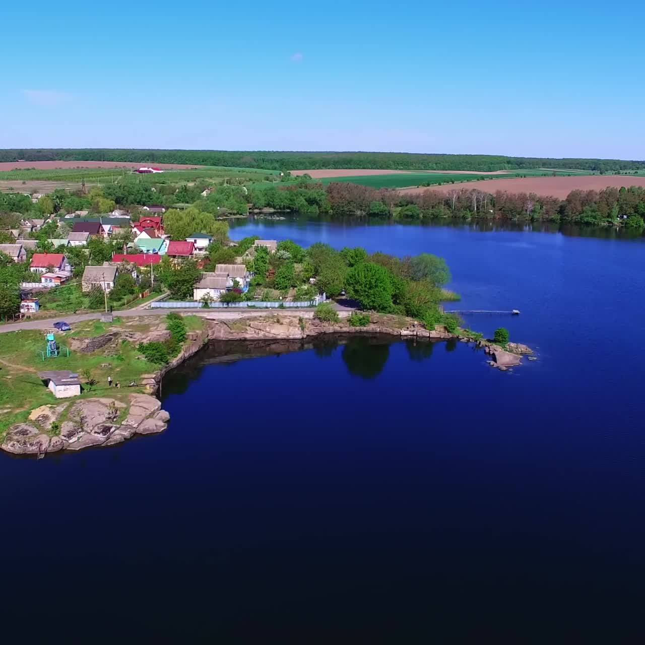 Contrasting azure surface of the river near the green bank. Cute cozy village with beautiful houses on bright sunny daytime from top