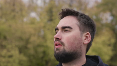 portrait of a bearded man breathing and looking around while standing at park in the morning