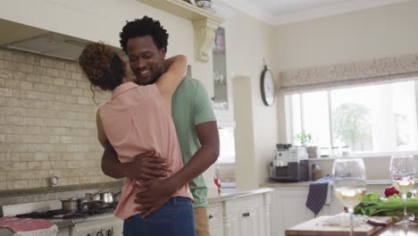 happy biracial couple hugging in kitchen while cooking