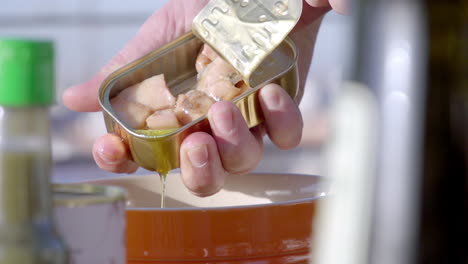 close-up of a person opening a tin can of fish, with the contents being revealed and oil dripping