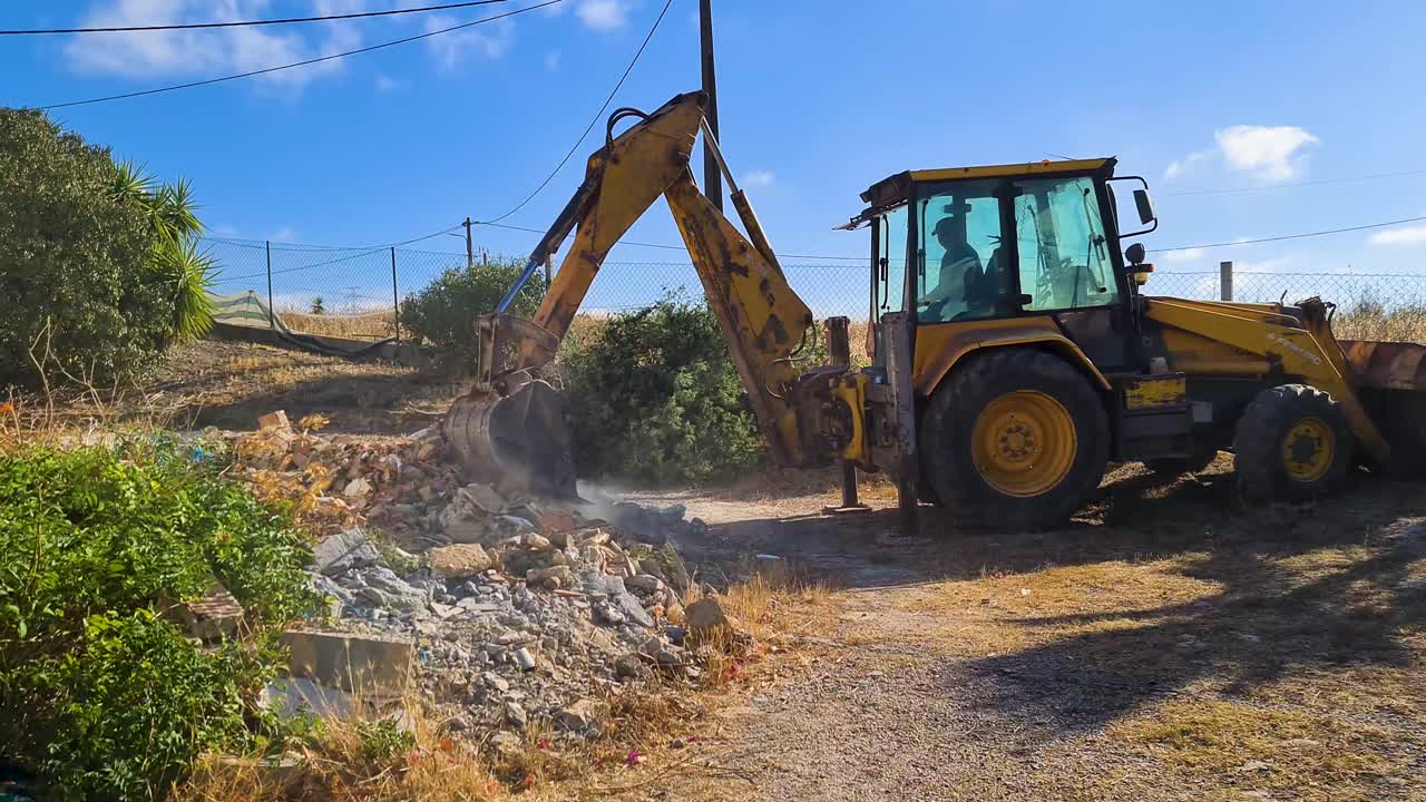 close up of an excavator cleaning the ground next to a house on a sunny day with a blue sky