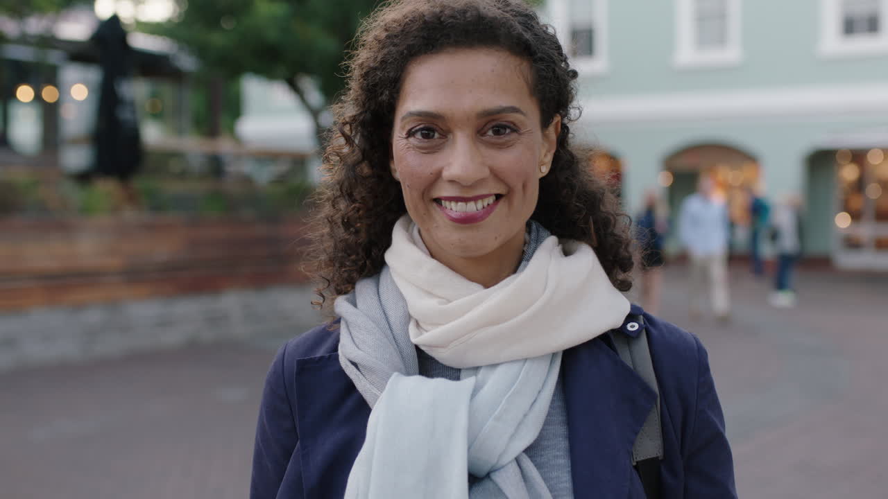 slow motion portrait of beautiful mixed race woman smiling confidently at camera in urban background wearing scarf