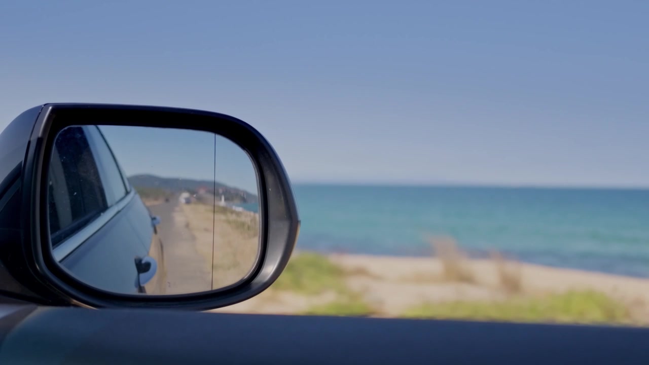 Car side mirror reflecting road beside sunny beach and sea horizon near to Sozopol, Burgas, Bulgaria