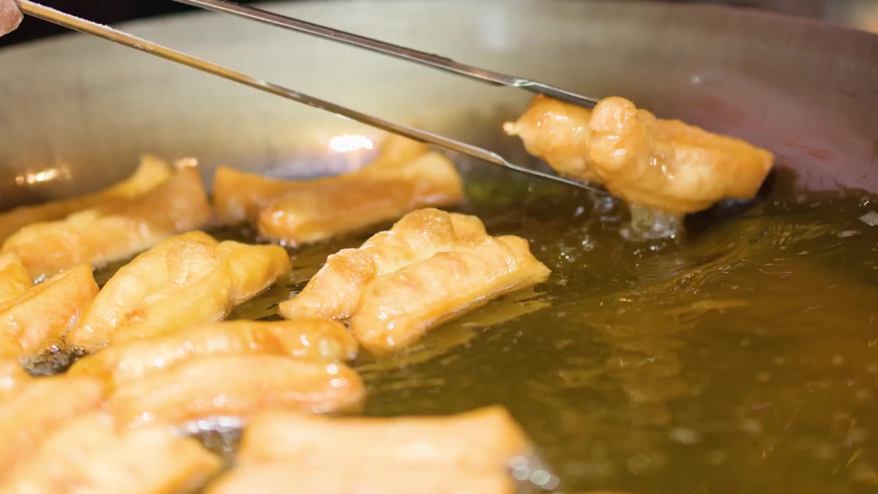 Close-up shot of golden dough sticks frying in hot oil and being turned with tongs.