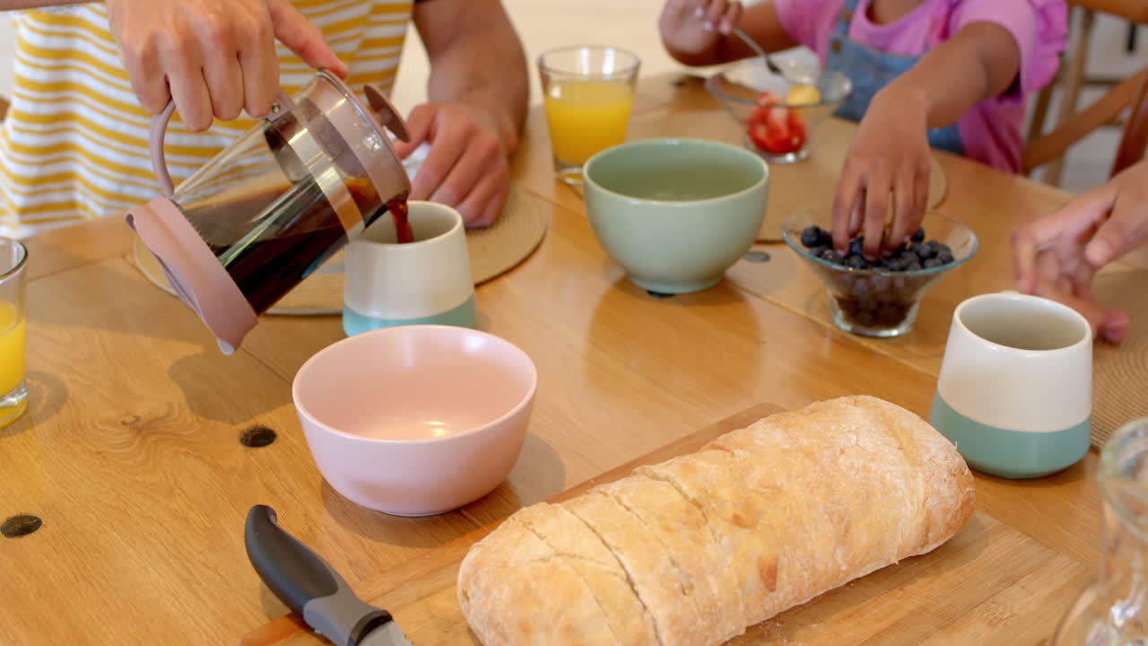 Famiglia che fa colazione insieme, versando il caffè e condividendo frutta fresca.
