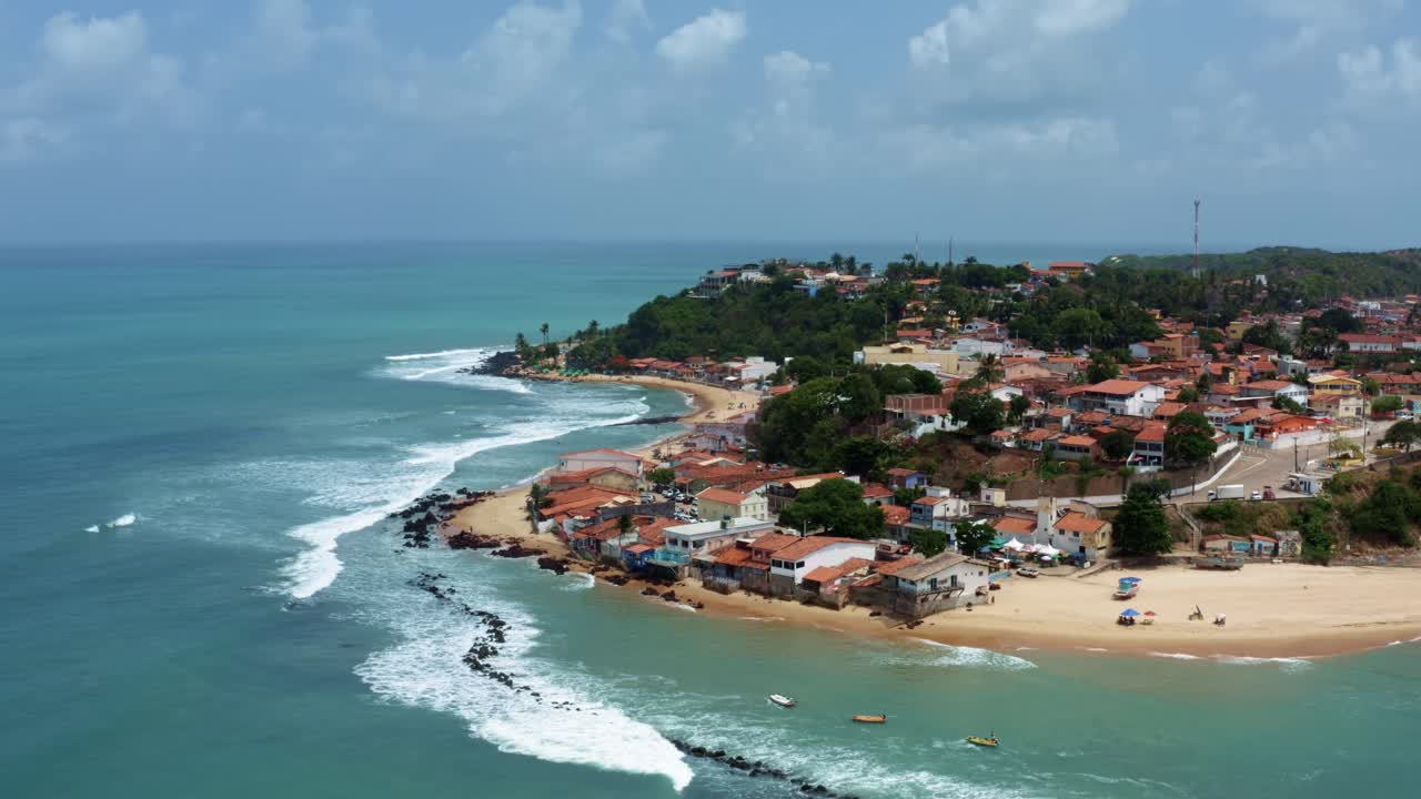 Rising, dolly out, tilt up aerial drone wide shot of the famous Baia Formosa beach town in the state of Rio Grande do Norte, Brazil with fishing boats, coastal homes, small waves, and sea birds