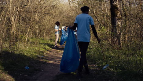 african american girl collecting rubbish in a trash bag using tongs