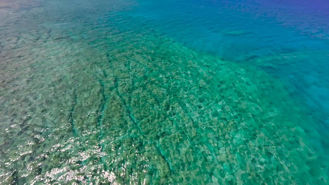 A sailboat glides smoothly across calm, clear blue waters. The scene captures the serenity of a sunny day at a stunning coastal spot, ideal for relaxation or adventure