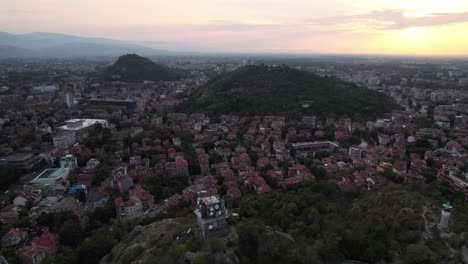 Paisaje-Urbano-De-Plovdiv-Con-Colinas-Cubiertas-De-Verde,-Puesta-De-Sol,-Vista-Aérea-De-Drones