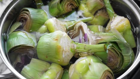 Put-and-cooking-artichokes-in-saucepan,-closeup-in-the-kitchen