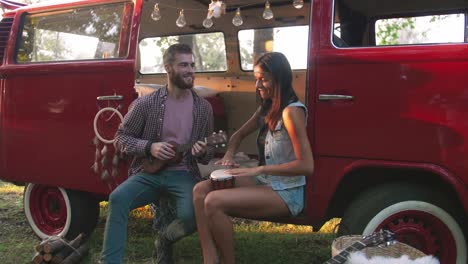 happy young mixed race couple playing instruments and having some fun in retro hippie minibus in forest