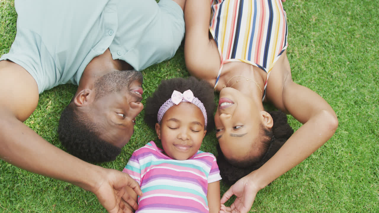 Ritratto di coppia afroamericana felice con la loro figlia sdraiati in giardino