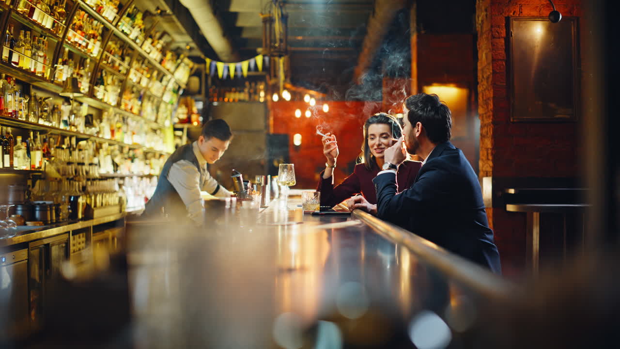 Casal fumando sentado no balcão do bar, compartilhando uma pausa para o cigarro. Um casal soltando fumaça.