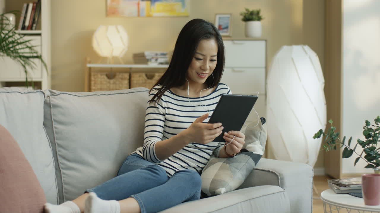 태블릿에서 무언가를 보고 거실에 있는 소파에 앉아 화면을 두드리는 젊은 여성