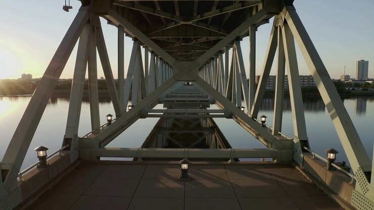 Moving camera initiating motion, revealing steel truss interior on deck, lamps and river reflecting