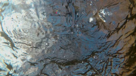 an unusual view from under the water on the surface of a fast river on which bubbles quickly float against the blue sky. an abstraction. hypnotic repeating pattern of waves. surreal realism. 4k.