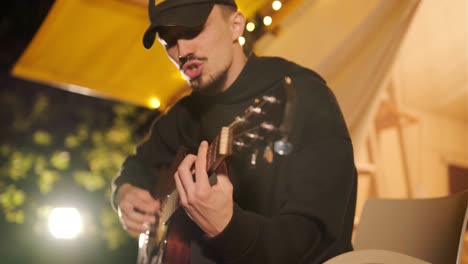 man plays the guitar and sings songs in a tent with light bulbs