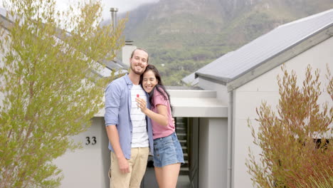 a young biracial couple is standing outside a new home showing key