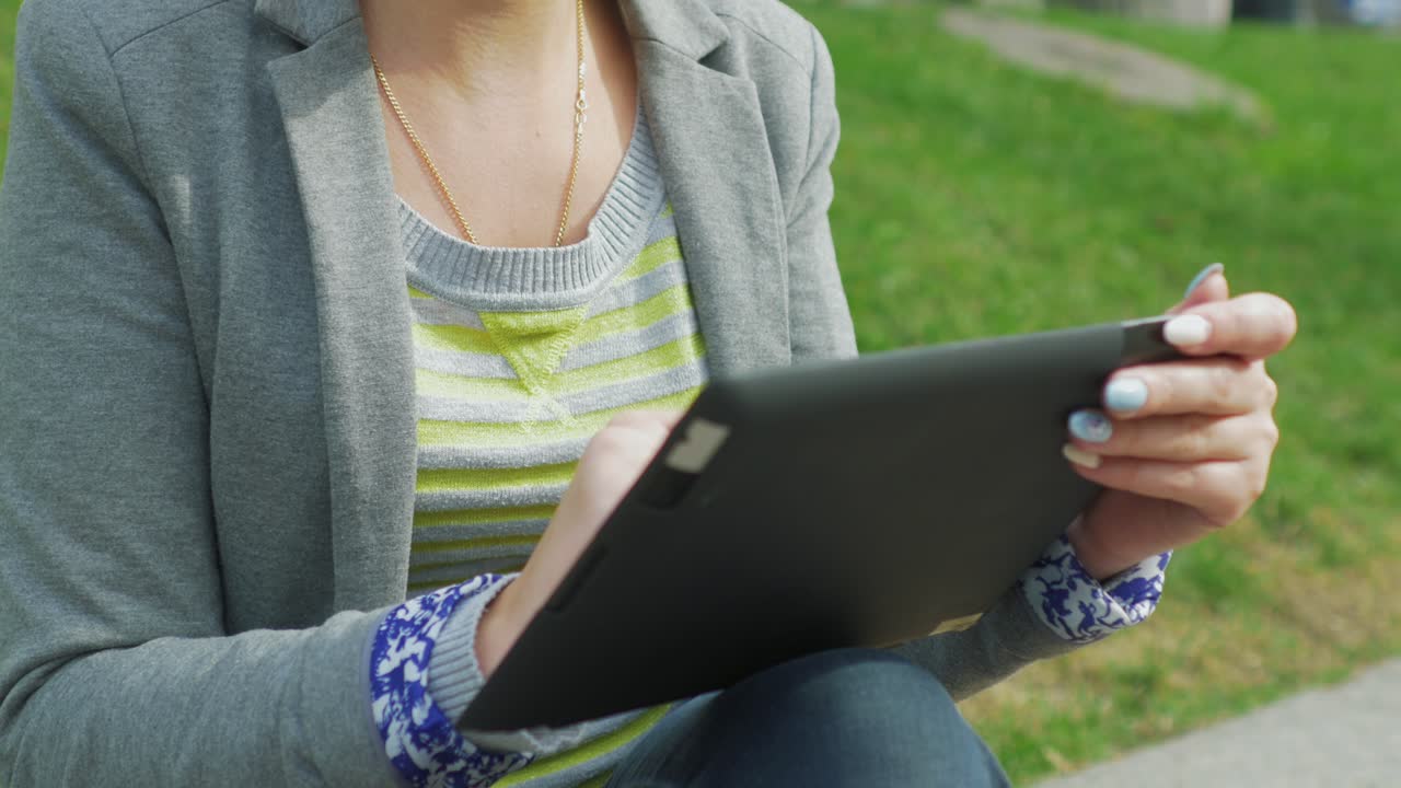 공원에서 쉬고 있는 젊은 여성은 디지털 태블릿 4k 비디오를 즐긴다