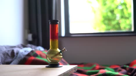 bong rojo y amarillo parado al lado de la cama, adicción a las drogas, rutina de hábitos recreativos