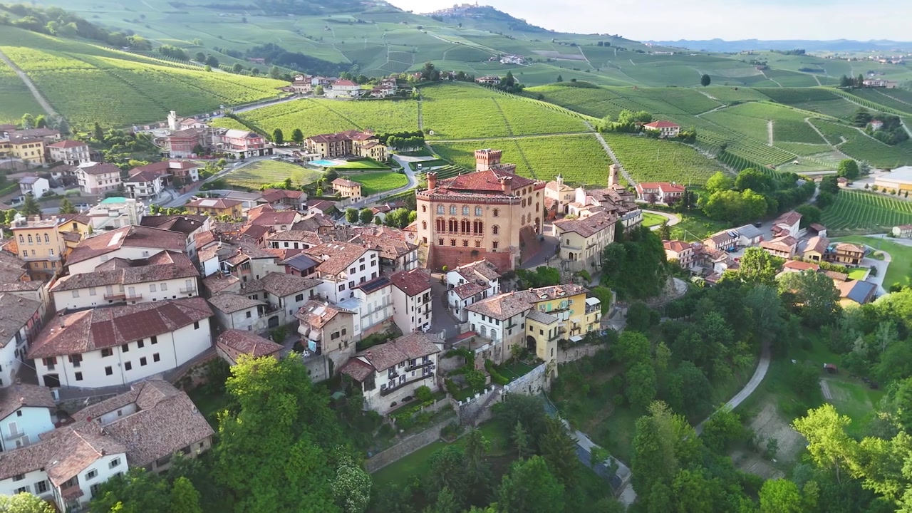 Ampia ripresa aerea con drone di uno storico borgo italiano circondato da dolci colline verdi di vigneti.