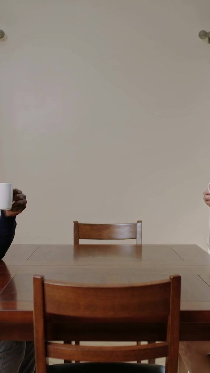Video vertical: Adultos con mangas largas moviendo tazas de los lados, sosteniendo tazas en la mesa de casa mientras hablan.