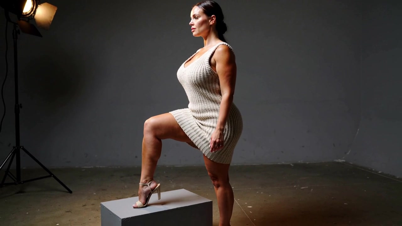 Posing model in beige-dress placing foot on gray box on cue for camera, with studio key-light