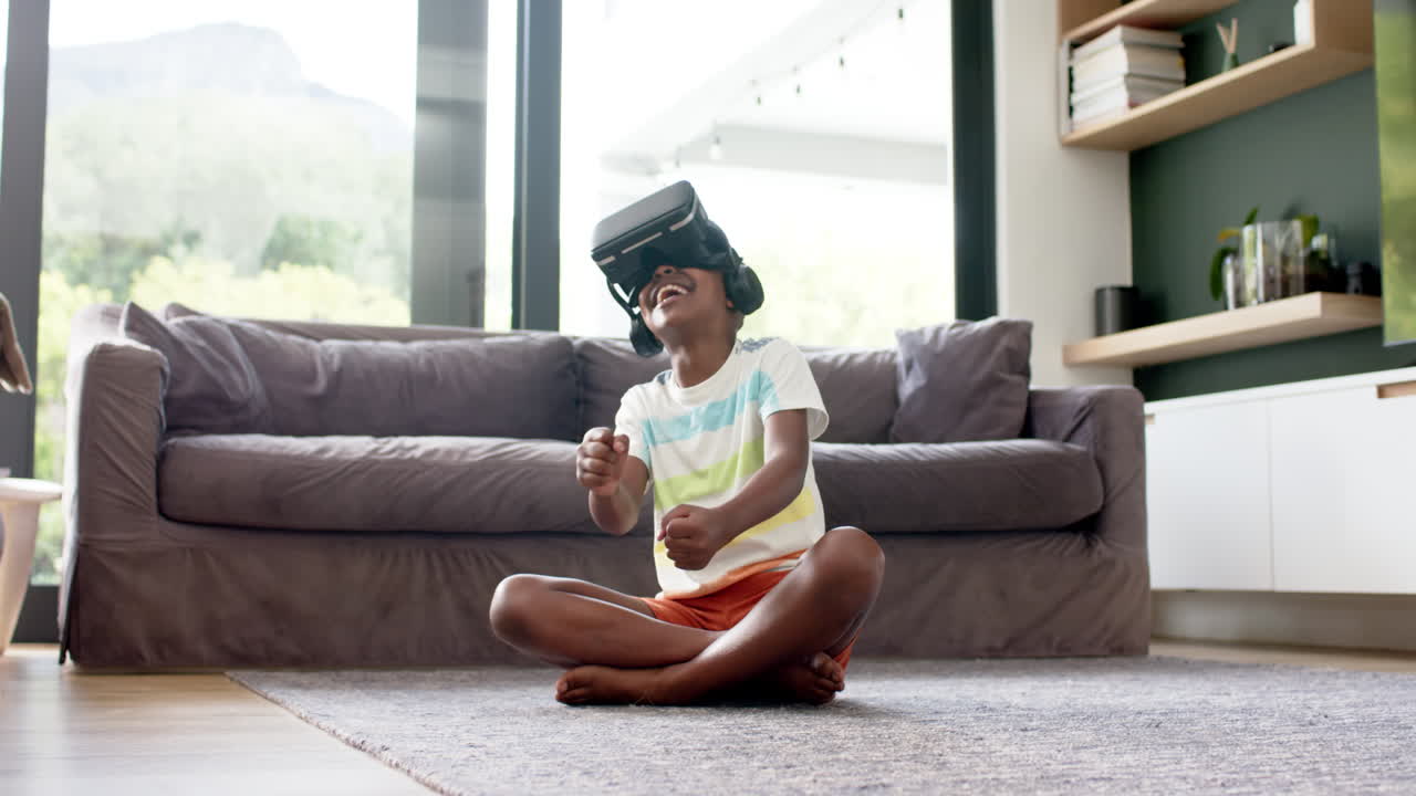 Happy african american boy in vr headsets playing with virtual interface, copy space, slow motion