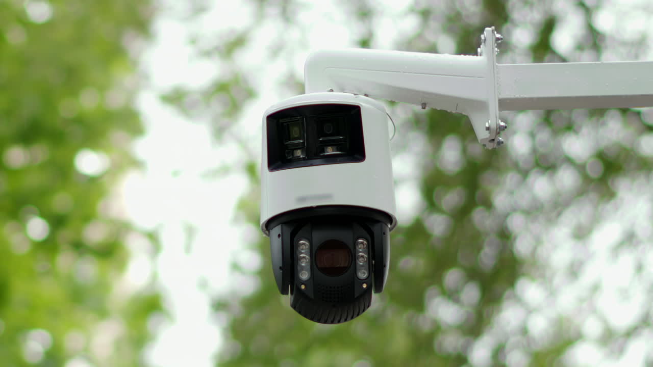Round, black and white surveillance camera on a stand with trees on the background