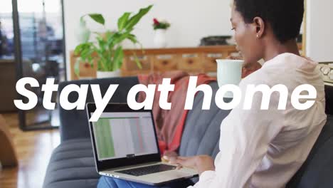 animation of stay at home text over african american woman using laptop at home