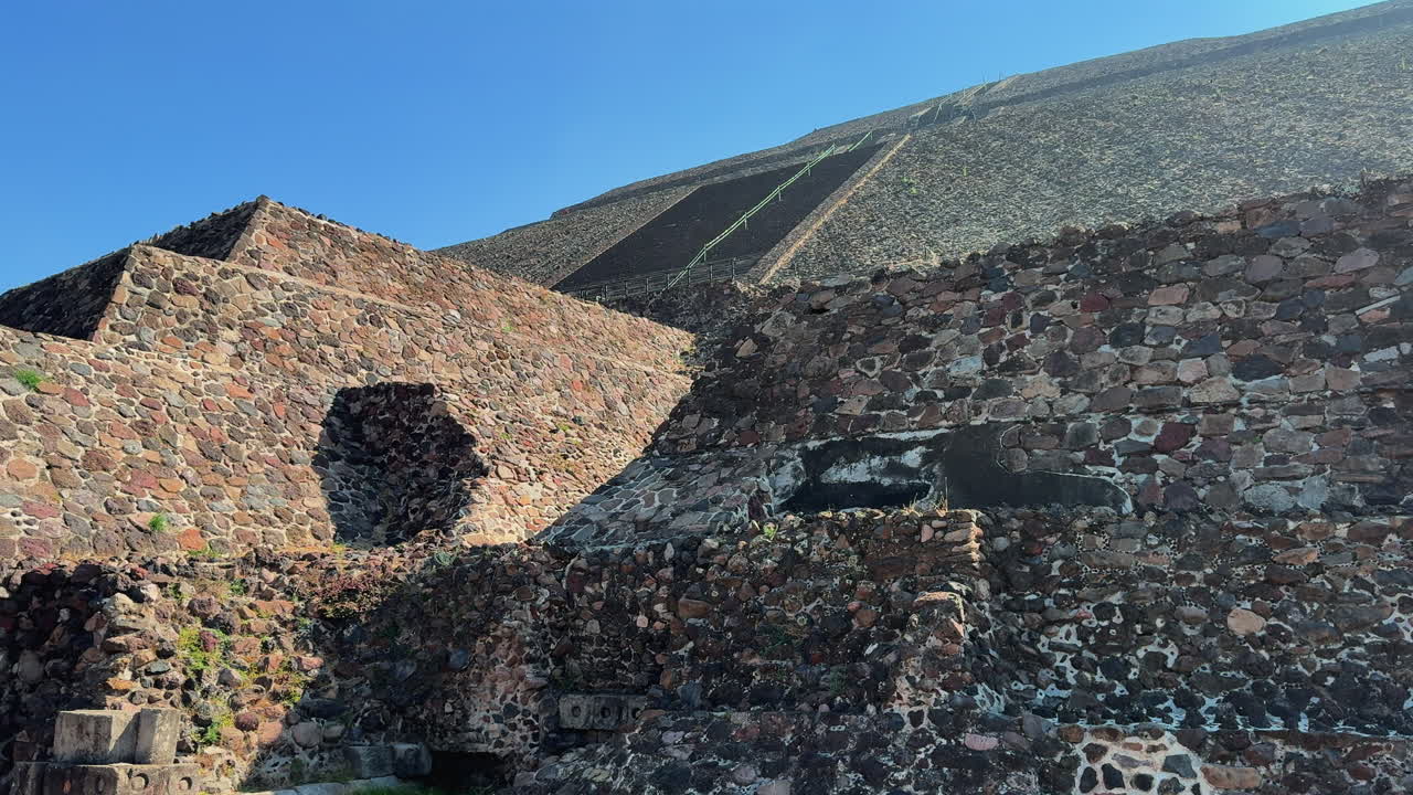 Teotihuacan Güneş Piramidi'nin taş terasları ve basamaklarının parlak güneş ışığında alçak açılı görünümü, berrak mavi gökyüzüne karşı dramatik gölgeler