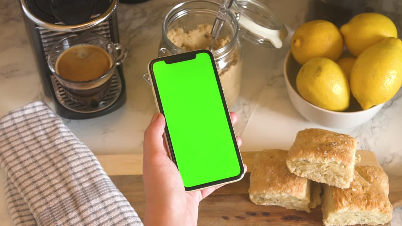 mujer sosteniendo un teléfono de pantalla verde en la cocina