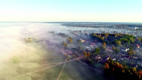 drone flies above morning mist at sunrise over small countryside town