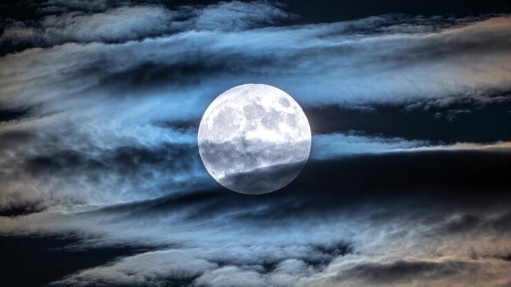 Faixas de nuvens flutuantes movendo-se sobre a lua cheia centralizada à noite, impulsionadas por um vento suave.