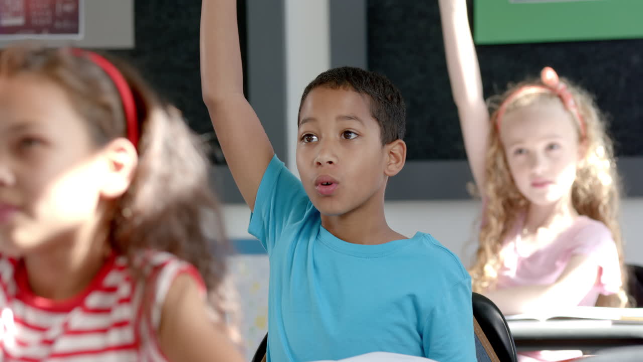 Biracial boy raises his hand eagerly in a classroom setting in school
