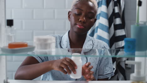 View-Through-Bathroom-Cabinet-Of-Young-Woman-Taking-Medication-From-Container