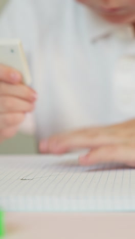 little boy swipes dirt after picture erasing from paper notebook page at table closeup. toddler child does art homework sitting at desk in children room