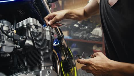 close-up shot of a man using his strong, sinewy hands to tighten a nut and repair a motorcycle using a hex tool in his garage workshop