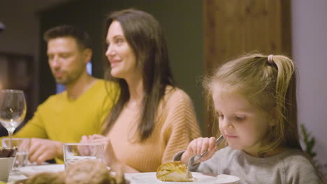 Seitenansicht-Eines-Blonden-Kleinen-Mädchens,-Das-Apfelkuchen-Isst-Und-Am-Tisch-Sitzt,-Während-Ihre-Eltern-Sie-Beim-Abendessen-Beobachten